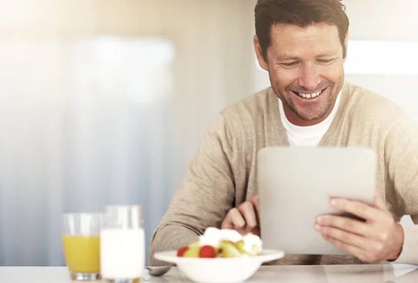 Przeglądam śniadanie. Przycięte ujęcie mężczyzny używającego tabletu podczas jedzenia śniadania w domu. — Zdjęcie stockowe