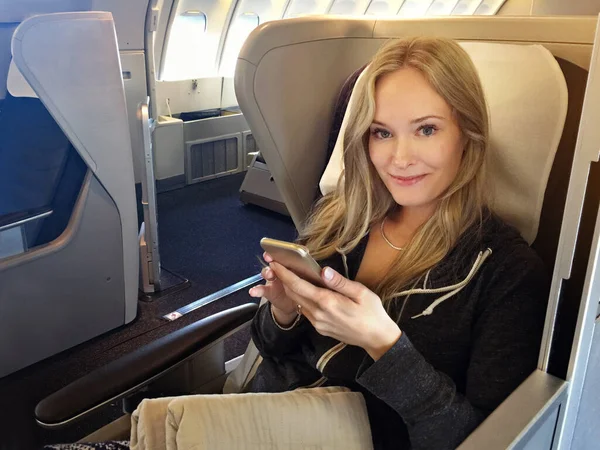 Modo avião. Retrato de uma jovem mulher usando seu celular enquanto sentada em primeira classe em um avião. — Fotografia de Stock