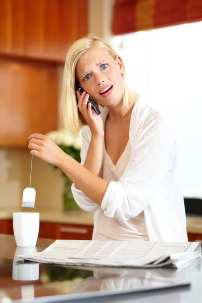 L'agitation de la vie moderne. Une charmante jeune femme prenant un appel téléphonique tout en faisant du thé et en lisant le journal. — Photo