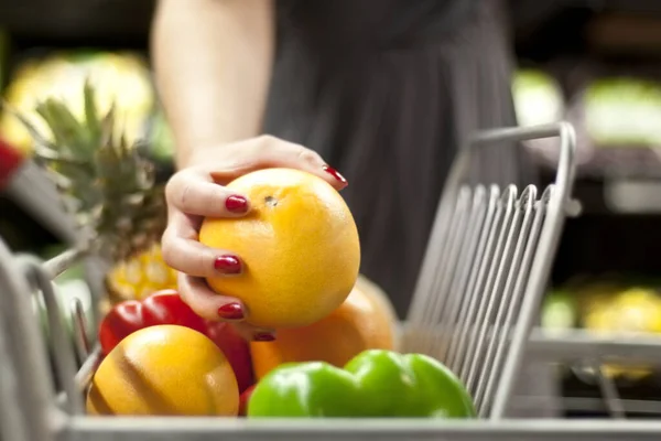 C vitamini almak için uzanan bir kadın, bir portakalı alışveriş arabasına yerleştiriyor.. — Stok fotoğraf