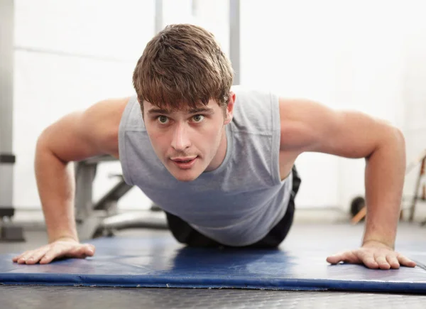 Perfeccionando su salud. Joven haciendo flexiones en una alfombra en un gimnasio. —  Fotos de Stock