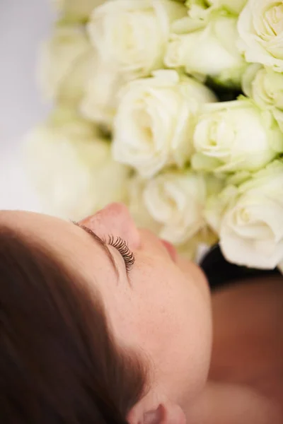Dingen van schoonheid. Een mooie jonge vrouw ligt met gesloten ogen en houdt een boeket witte rozen tegen haar borst. — Stockfoto
