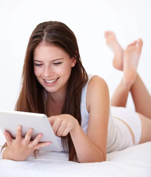 침대에서 편하게 인터넷을 하고 있어. 디지탈 태블릿으로 일하고 있는 아름다운 젊은 여성. — 스톡 사진