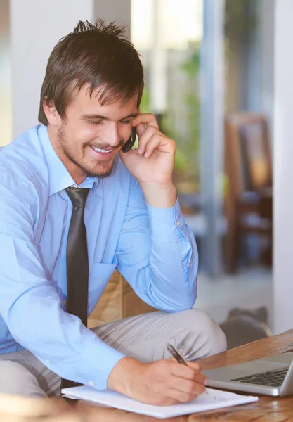Une bonne journée pour les affaires. Prise de vue d'un jeune homme d'affaires parlant au téléphone assis devant son ordinateur portable. — Photo