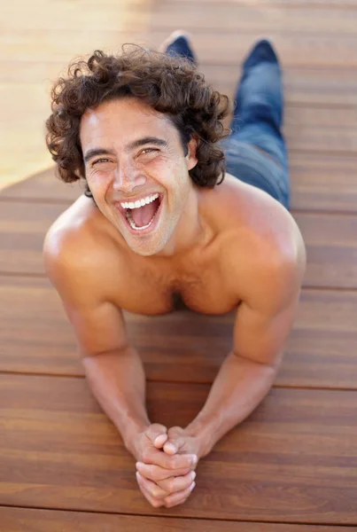 Το γέλιο κρατά τη ζωή ανάλαφρη. Πορτραίτο ενός σέξι νεαρού άντρα που ξαπλώνει σε ξύλινο πάτωμα. — Φωτογραφία Αρχείου