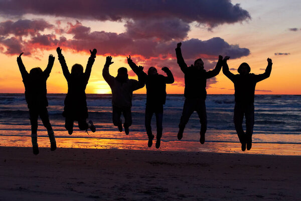 Experiencing the awesomeness of nature. Silhouette of a group of people jumping on the beach at sunset.