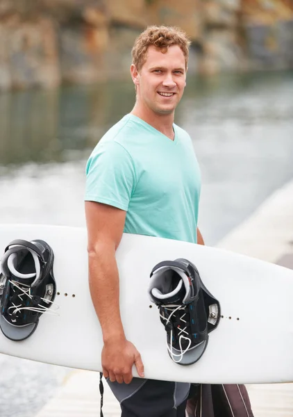 Ő egy buzgó wakeboardos. Mosolygó wakeboardos kezében a wakeboard mellett a tó. — Stock Fotó