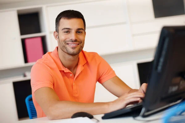 Il aime son travail. Un jeune entrepreneur souriant travaillant à son ordinateur. — Photo