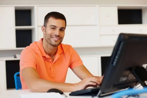 Il aime son travail. Un jeune entrepreneur souriant travaillant à son ordinateur. — Photo