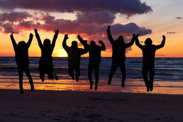 Experiencing the awesomeness of nature. Silhouette of a group of people jumping on the beach at sunset. Stock Photo