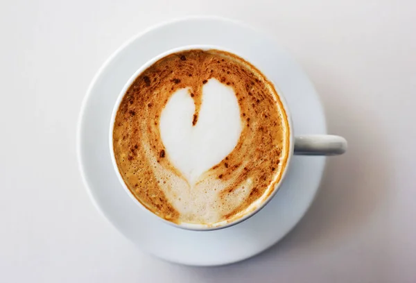 Le meilleur début de matinée. Un cappuccino fraîchement préparé sur une table blanche en forme de cœur dans la mousse de lait. — Photo