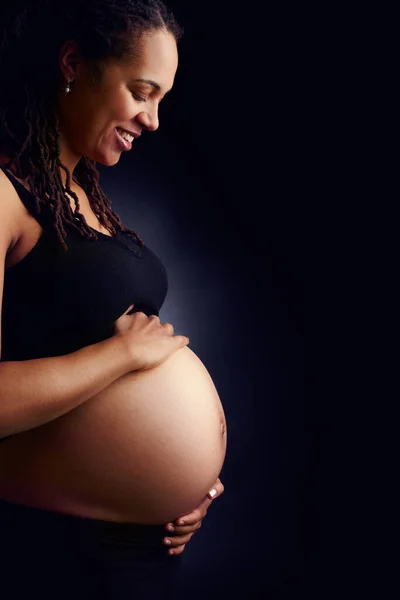 O meu bebé está a crescer. Um perfil lateral de uma mulher grávida tranquila segurando sua barriga nua e olhando para baixo. — Fotografia de Stock