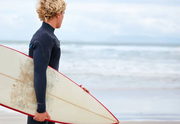 Auf der Suche nach der perfekten Welle... Ein junger Surfer steht am Strand, im Hintergrund das Meer. — Stockfoto