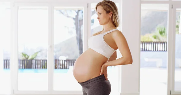 Η πλάτη σου δέχεται μεγάλη πίεση κατά τη διάρκεια της εγκυμοσύνης. Ζωγραφισμένο πορτραίτο μιας ελκυστικής νεαρής εγκύου που στέκεται με τα χέρια στην πλάτη της. — Φωτογραφία Αρχείου