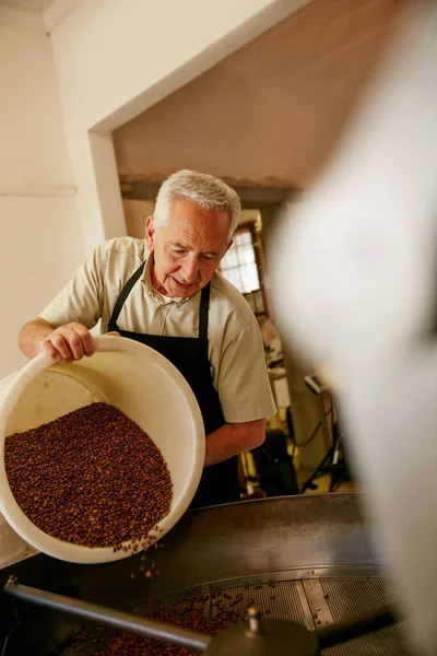 Llenando el tostador. Fotografía recortada de un hombre mayor trabajando en un roasterio. — Foto de Stock