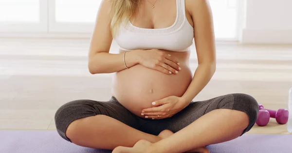 In goede handen. Gehakt schot van een onherkenbare jonge zwangere vrouw wrijven haar baby hobbel terwijl zitten op een yoga mat. — Stockfoto