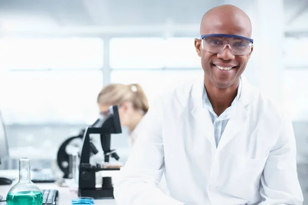 Ricercatore sorridente. Ritratto di un giovane chimico sorridente in laboratorio con una collega sullo sfondo. — Foto Stock
