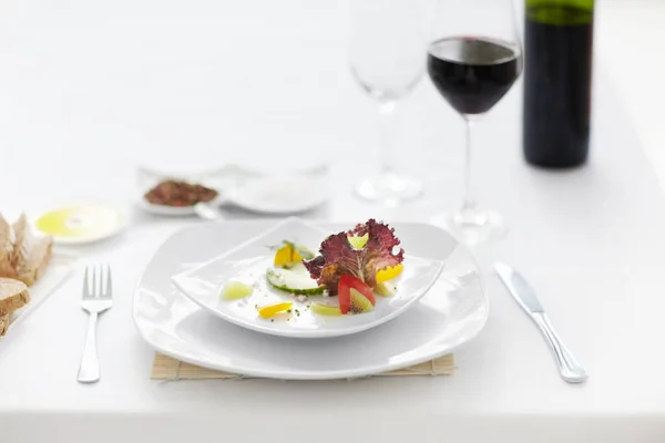 Het beeld van lekker eten. Een prachtig bereide salade vergezeld van een glas wijn op een witte tafelschikking. — Stockfoto