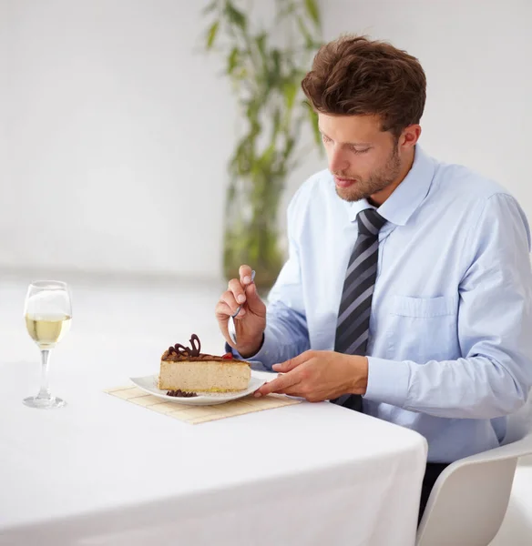 他有一颗甜食。一个英俊的年轻人在餐馆里吃着一块美味的芝士蛋糕. — 图库照片