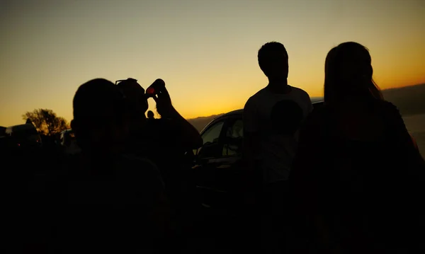 Terminando el día con una hermosa puesta de sol. Silueta de un grupo de amigos contra una puesta de sol amarilla. — Foto de Stock
