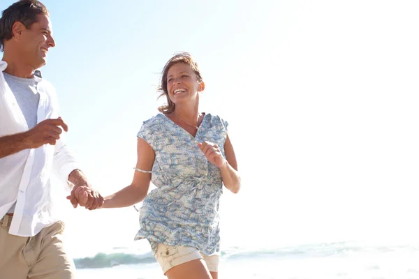 Бути на пляжі змушує вас почуватися молодими знову. Щаслива зріла пара тримає руки під час бігу на пляжі . — стокове фото