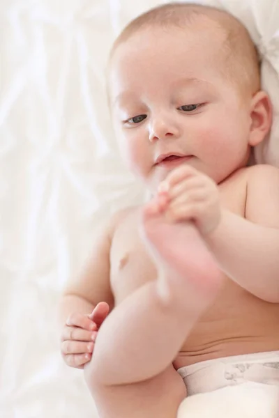 Learning through play. Sweet little baby lying down and touching its feet. — Stock Photo, Image