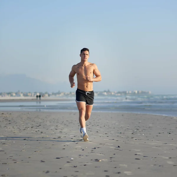 Ślady. Pełne ujęcie przystojnego młodego mężczyzny biegającego po plaży. — Zdjęcie stockowe