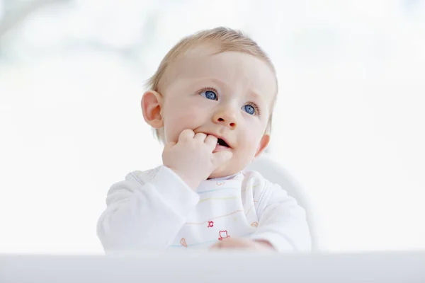 Curious about everything. A cute baby boy sitting in his high chair with his fingers in his mouth. — Stock Photo, Image