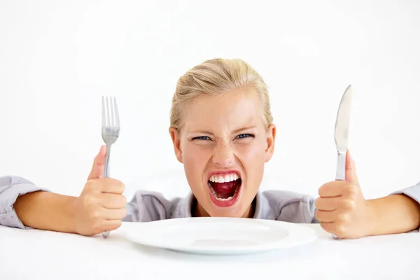 Dit is belachelijk. Ik sterf van de honger. woedende jonge vrouw zittend voor een leeg bord terwijl ze haar mes en vork vasthoudt. — Stockfoto