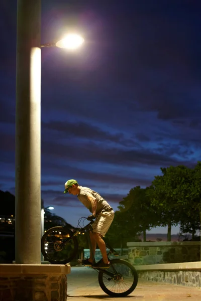 잠 도자지 말고 그냥 타 보 세요. 한 남자가 밤에 자전거를 타고 길거리 불빛 아래서 트릭을 하는 모습을 찍은 사진. — 스톡 사진