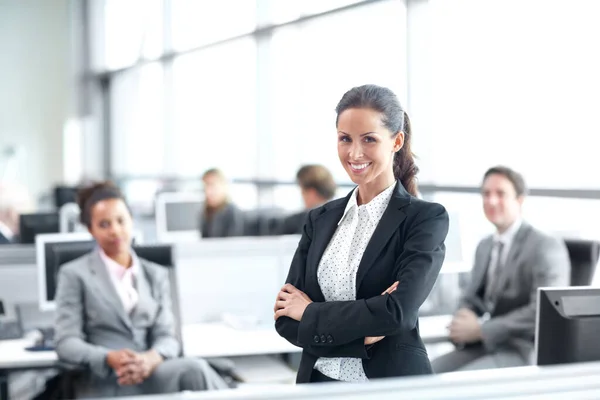 Positive sur sa carrière dans l'entreprise. Jolie jeune femme d'affaires debout avec confiance dans le bureau avec ses collègues derrière elle - portrait. — Photo