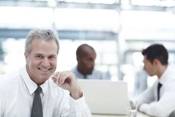 C'est un employeur équilibré. Portrait d'un homme d'affaires mature souriant assis devant deux jeunes collègues. — Photo