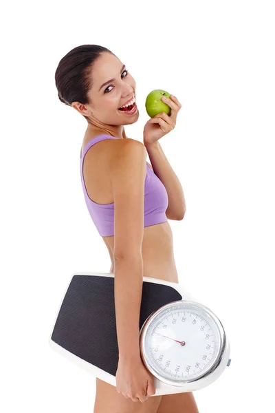 改变她的饮食习惯意味着减肥。一个穿着运动服、拿着苹果和秤的年轻貌美女子的演播室照片. — 图库照片