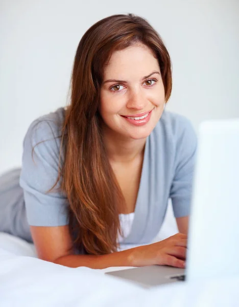Yataktayken dizüstü bilgisayar kullanan mutlu bir kadın. Yatakta rahat bir şekilde yatarken dizüstü bilgisayar kullanan genç bir kadının portresi.. — Stok fotoğraf