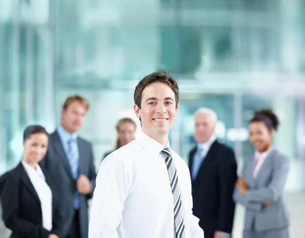 Estoy rodeado de excelentes modelos corporativos a seguir. Guapo joven socio de negocios sonriendo con sus colegas en el fondo - retrato. —  Fotos de Stock