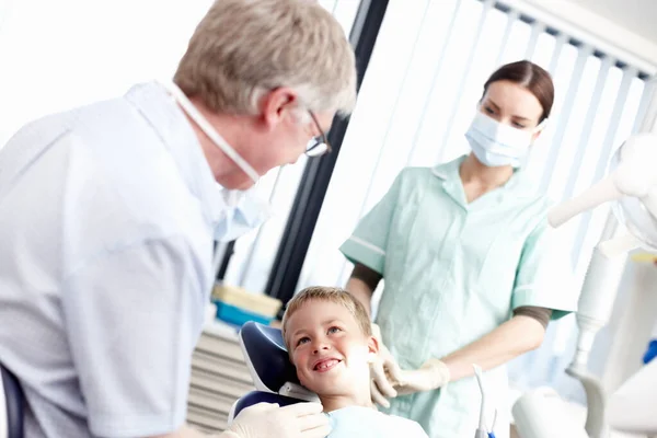 Dental treatment clinic. Portrait of young boy smiling at dentist with assistant in office. — Stock Photo, Image