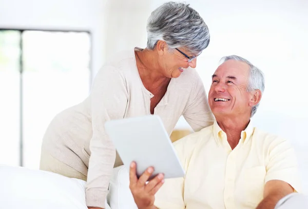 Cheerful mature couple using tablet PC. Cheerful mature couple smiling while using tablet PC at home. — Stock Photo, Image
