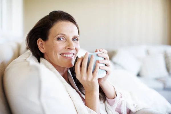 A fazer uma pausa para o café em casa. Retrato de uma mulher atraente desfrutando de uma xícara de café enquanto sentado em um sofá dentro de casa. — Fotografia de Stock