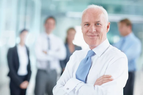 Orgulloso de la carrera que he tallado para mí. Smiling senior businessman standing with his team in the background - retrato. —  Fotos de Stock