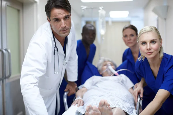 Mit ihr in den OP. Porträt einer Gruppe von Ärzten, die einen Patienten den Flur hinunterdrücken. — Stockfoto