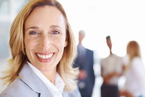 Sonriente profesional femenina con asociados. Primer plano de profesional femenina madura sonriendo con asociados en segundo plano. —  Fotos de Stock