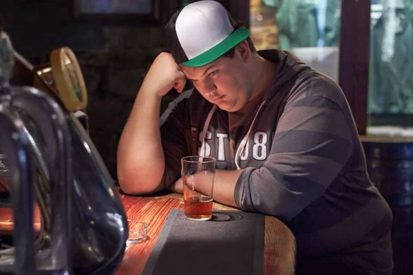 Het leven brengt je naar beneden. Een jonge man ziet er eenzaam uit aan de bar.. — Stockfoto
