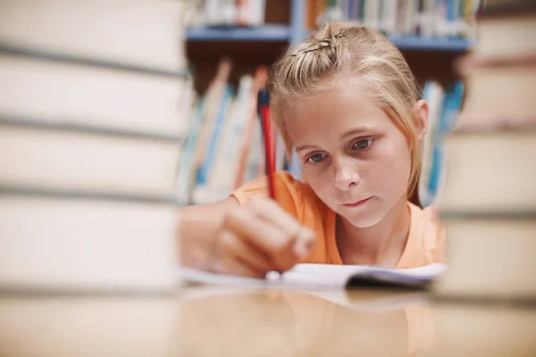Hard aan het werk. Een schattig jong meisje doet schoolwerk terwijl omringd door boeken in de bibliotheek. — Stockfoto