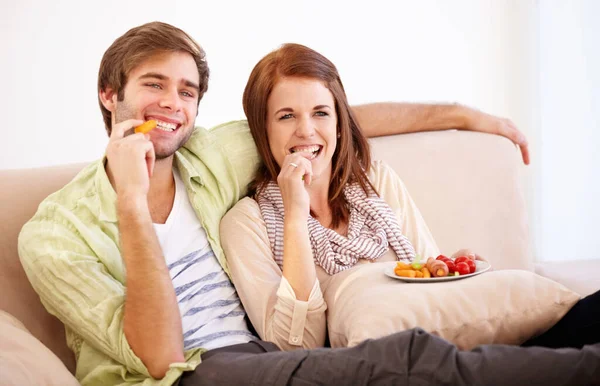 Détente avec de la bonne nourriture et une meilleure compagnie. Un jeune couple se relaxant sur le canapé avec une collation saine. — Photo