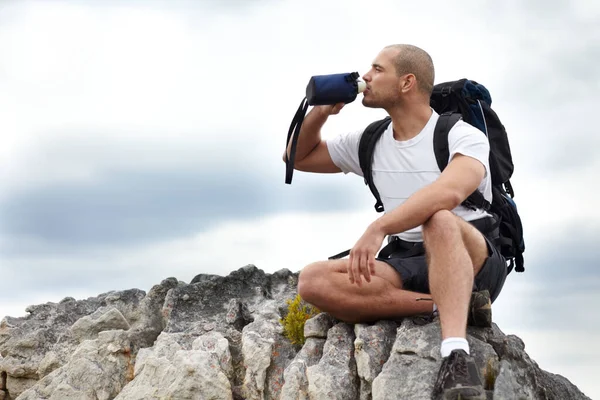 Tomar el camino menos recorrido. Un joven tomando un descanso del senderismo mientras está sentado en una roca y bebiendo un poco de agua. — Foto de Stock
