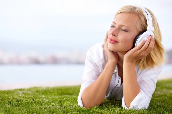 Ze neemt haar muziek overal mee naartoe... Shot van een vrouw liggend op een grasveld luisterend naar muziek met haar ogen dicht. — Stockfoto