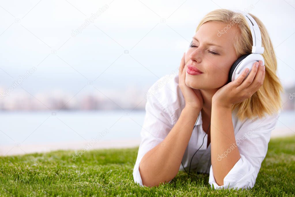 Taking her music everywhere.... Shot of a woman lying on a grassy field listening to music with her eyes closed.