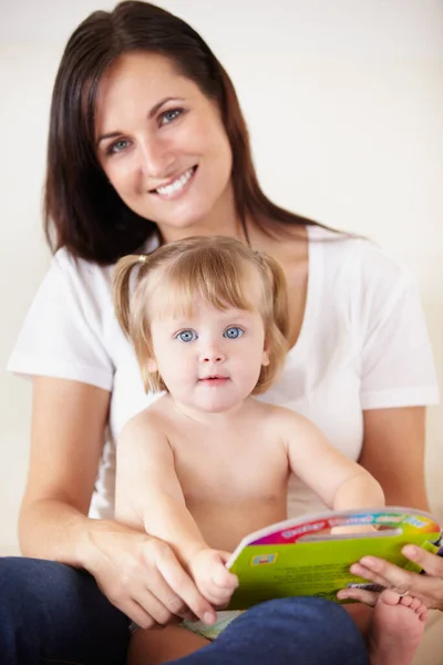 Vorlesen für ihr kleines Mädchen. Ein süßes kleines Mädchen sitzt mit einem Buch auf dem Schoß ihrer Mutter. — Stockfoto