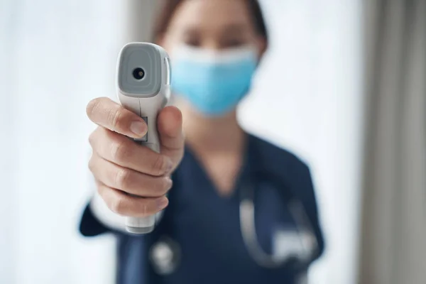Temperatuurcontroles zijn belangrijk tijdens deze pandemie. Schot van een jonge vrouwelijke arts die een thermometer in een kantoor wijst. — Stockfoto