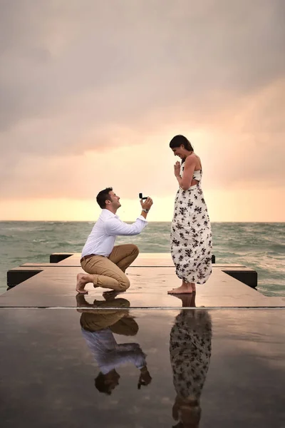 Auf einem Knie runterkommen. Aufnahmen in voller Länge von einem hübschen jungen Mann, der seiner Freundin auf dem Steg am Strand einen Heiratsantrag macht. — Stockfoto
